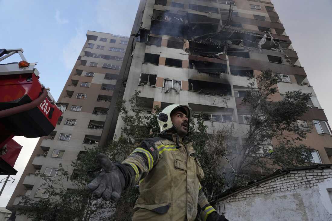 A firefighter calls out his colleagues at the scene of an explosion in a residence compound in northern Tehran, Iran, Friday, June 13, 2025. (AP Photo/Vahid Salemi)